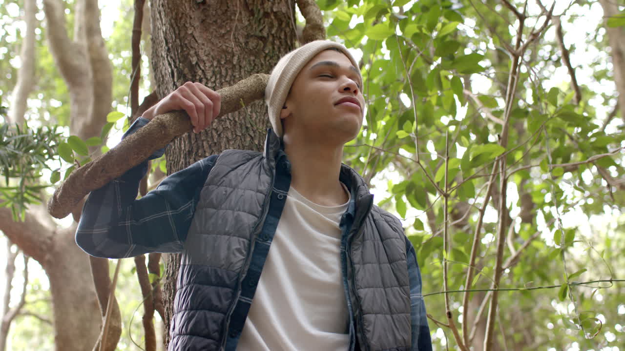 Young man enjoying nature, leaning against tree in peaceful forest setting