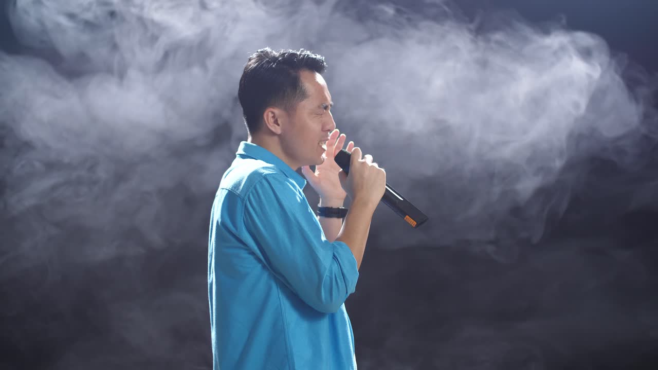 hombre cantando en un micrófono en un escenario con humo