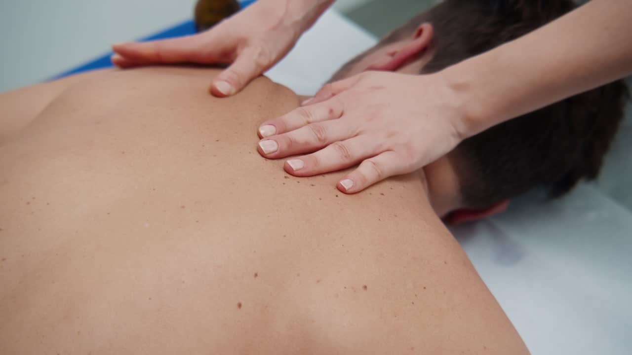 Il terapista applica pressione sulla parte alta della schiena e sulle spalle di un uomo durante un massaggio in un ambiente clinico
