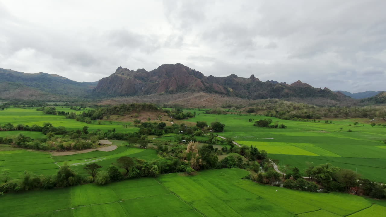 Aerial view of green field and rocky mountain with cloudy sky during daytime in 4K quality