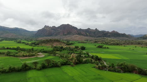 Aerial-view-of-green-field-and-rocky-mountain-with-cloudy-sky-during-daytime-in-4K-quality