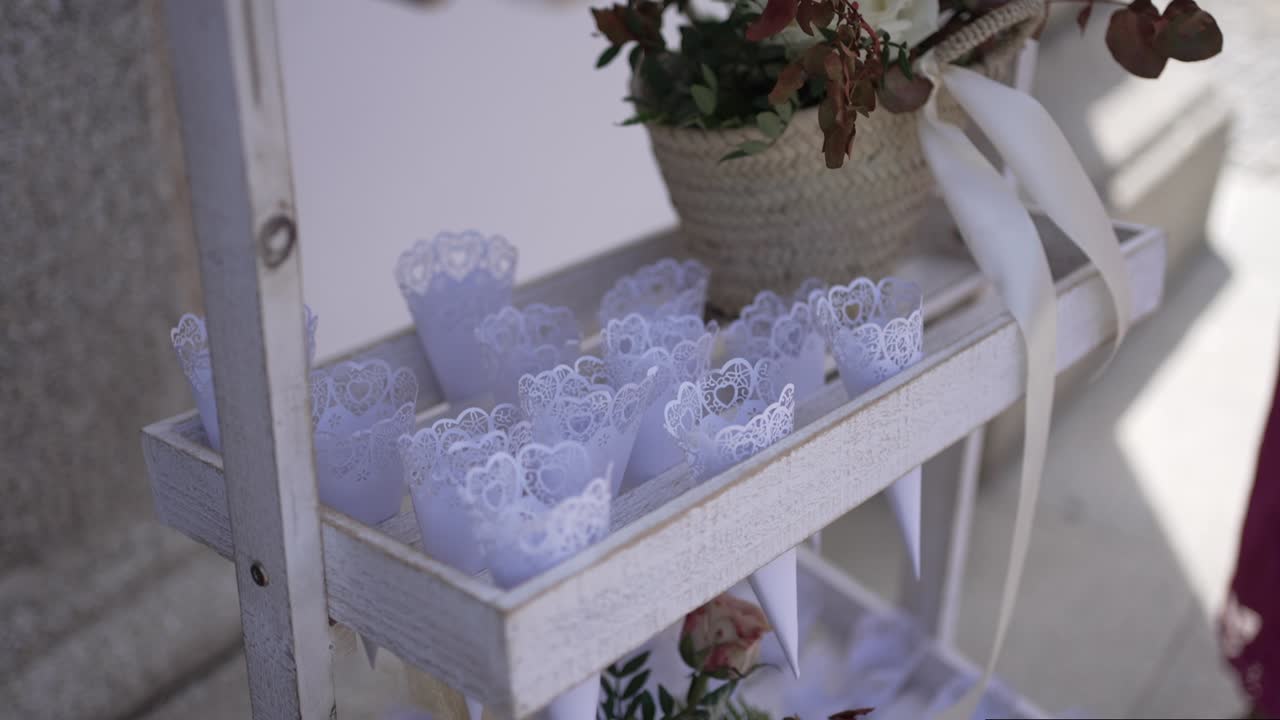 estante decorativo blanco con conos de encaje y una canasta de flores, ideal para un entorno de boda