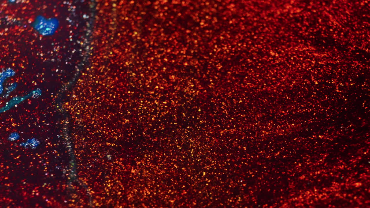 Macro view of shimmering green and blue ink as red ink is poured over it, creating a vivid and dynamic blend of colors