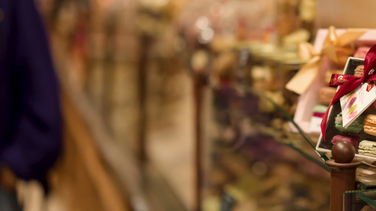Colorful macarons in gift boxes, bakery display case, warm lighting, slow camera pan, Bruges