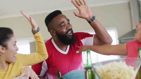happy diverse female and male friends watching football on tv high fiving, in slow motion