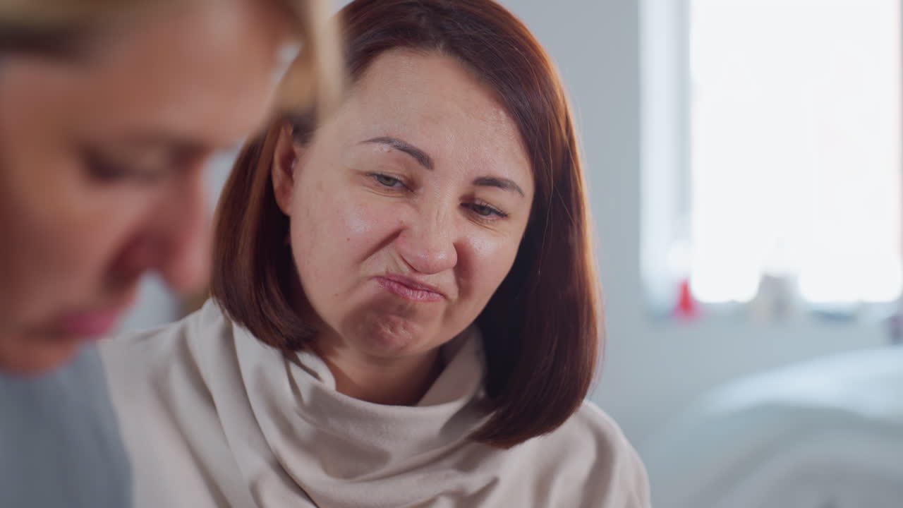 Close up of woman making funny face during lively conversation with friend indoors, showing playful expression with raised eyebrows and smirk while maintaining cheerful communication