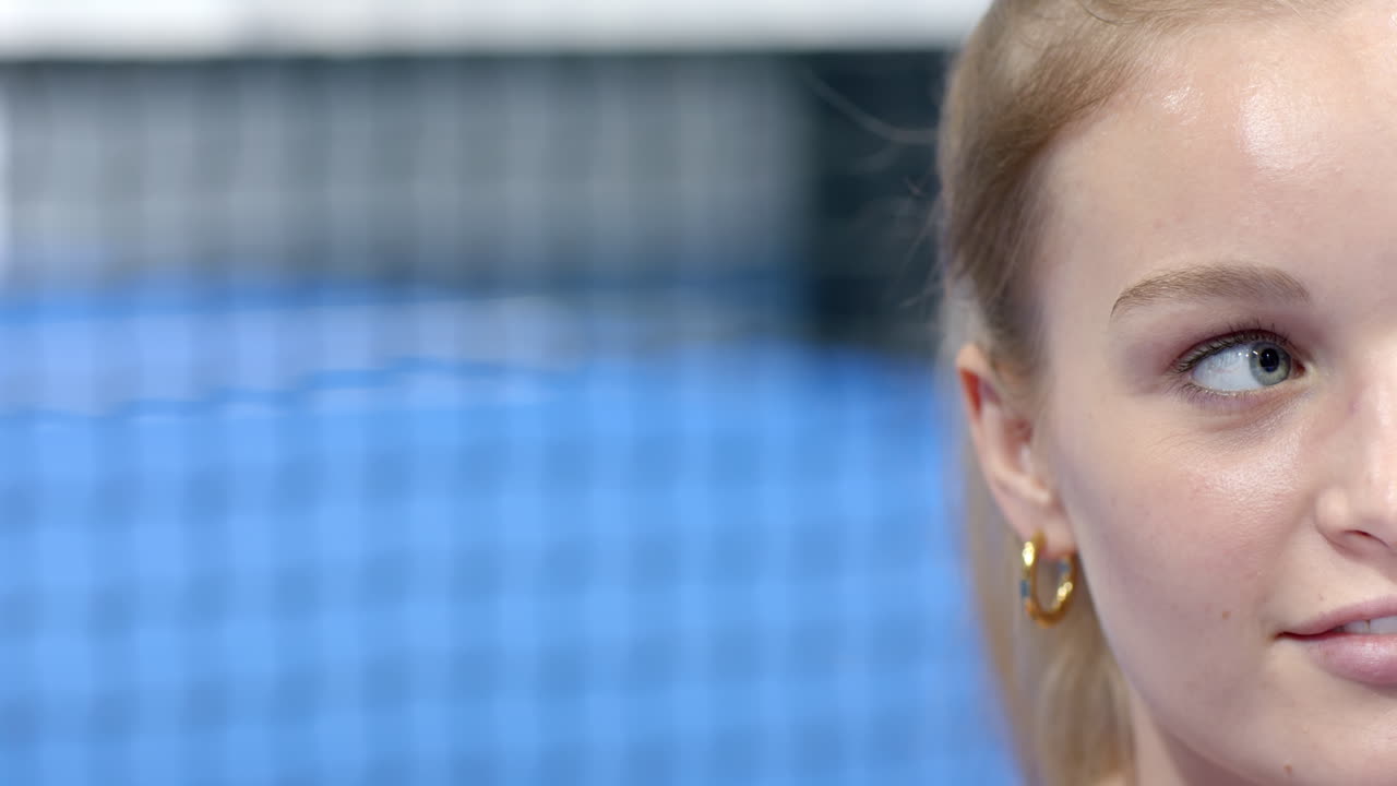Woman with blonde hair playing padel tennis, concentrating on game, at indoor court, copy space