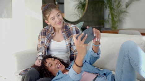 taking selfie, smiling lesbian couple relaxing together on couch at home
