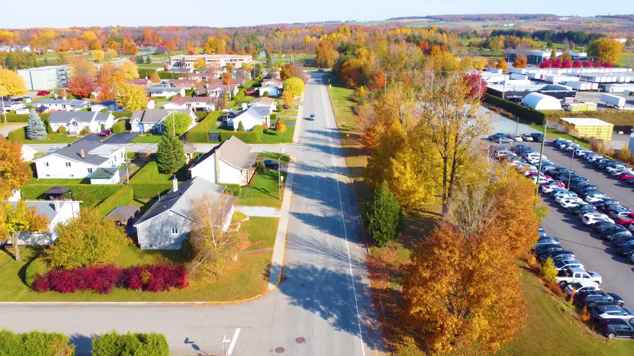 Drone shot of small village in Estrie, Quebec, Canada during fall months with autumn leaves changing colors. Warehouse and factory in the background