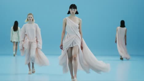 a captivating fashion showcase featuring models elegantly strutting on a serene blue stage, draped in ethereal pastel garments that exude modern sophistication and style