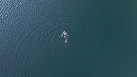 Drohnenaufnahmen-Von-Oben-Nach-Unten-Einer-Person,-Die-In-Einem-See-Schwimmt-Und-Der-Kamera-Ein-Zeichen-Gibt