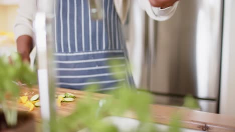 Mid-section-of-african-american-senior-woman-composting-vegetables-waste-in-kitchen,-slow-motion