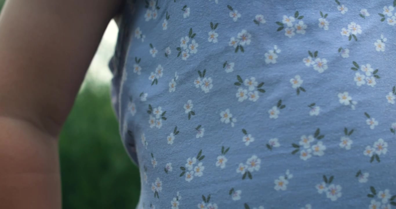 Nærbillede af en ung piges lyseblå kjole med blomstermønstre. Den bløde tekstur fremkalder en blid sommeræstetik.