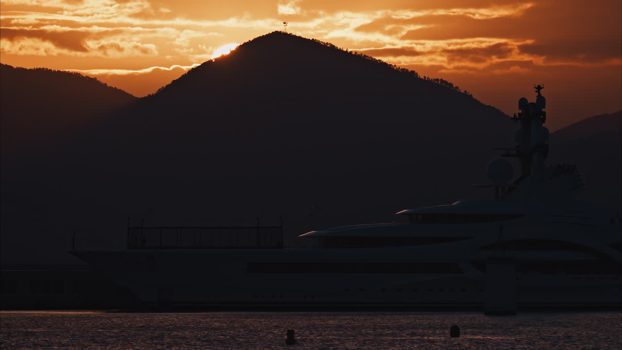 Distant view of a yacht docked on the sea with a mountain on the background at sunset
