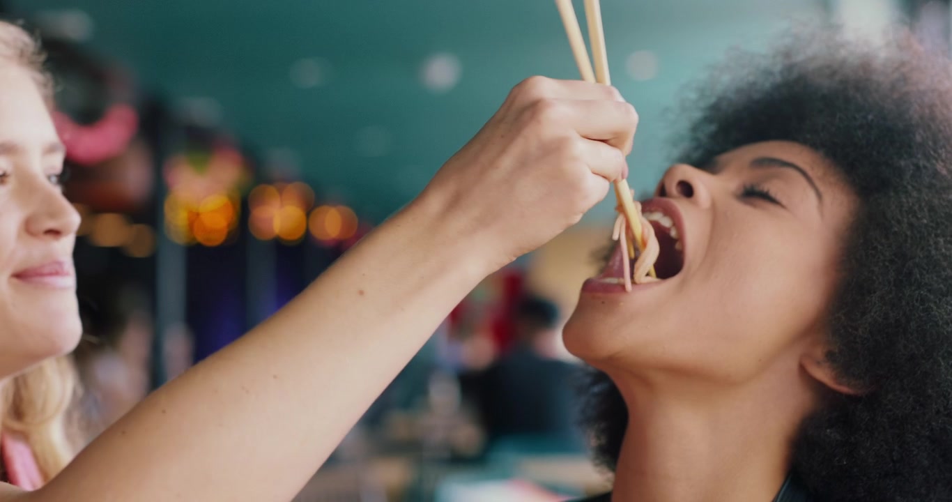 Giovane donna che dà da mangiare noodles alla sua amica con le bacchette in un ristorante