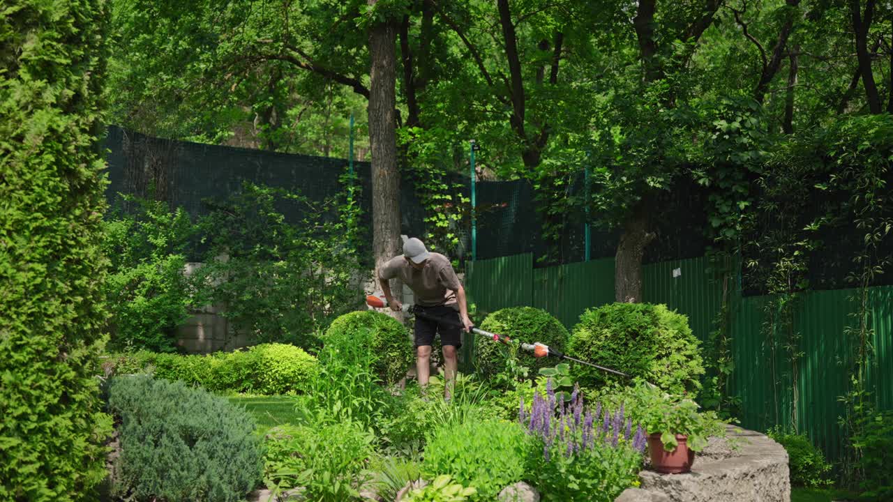 Man Trimming Bushes with a Long-Handled Hedge Trimmer in a Green Garden