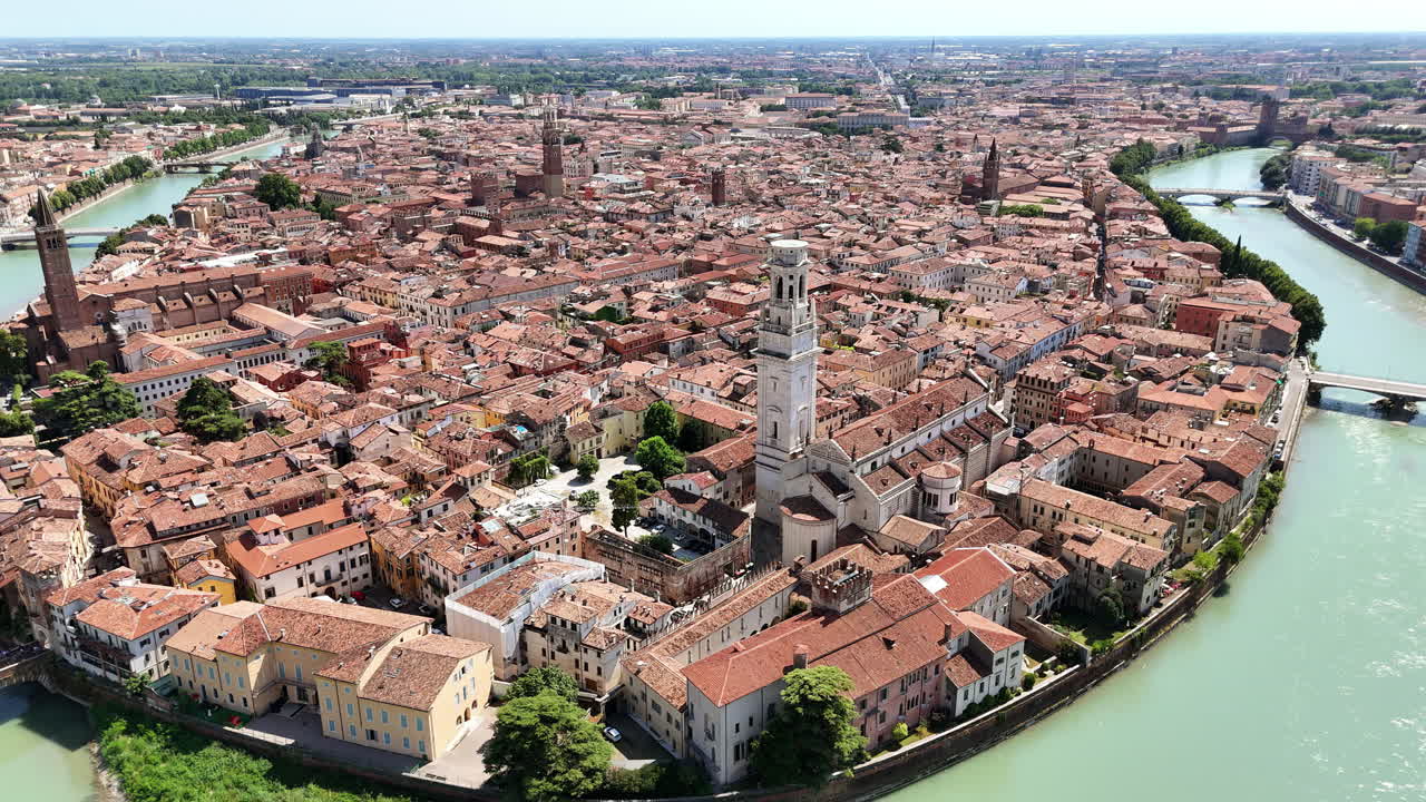 Aerial drone view of Verona's historic city center surrounded by the curved Adige River. The Verona Cathedral bell tower rises above red rooftops and historic architecture