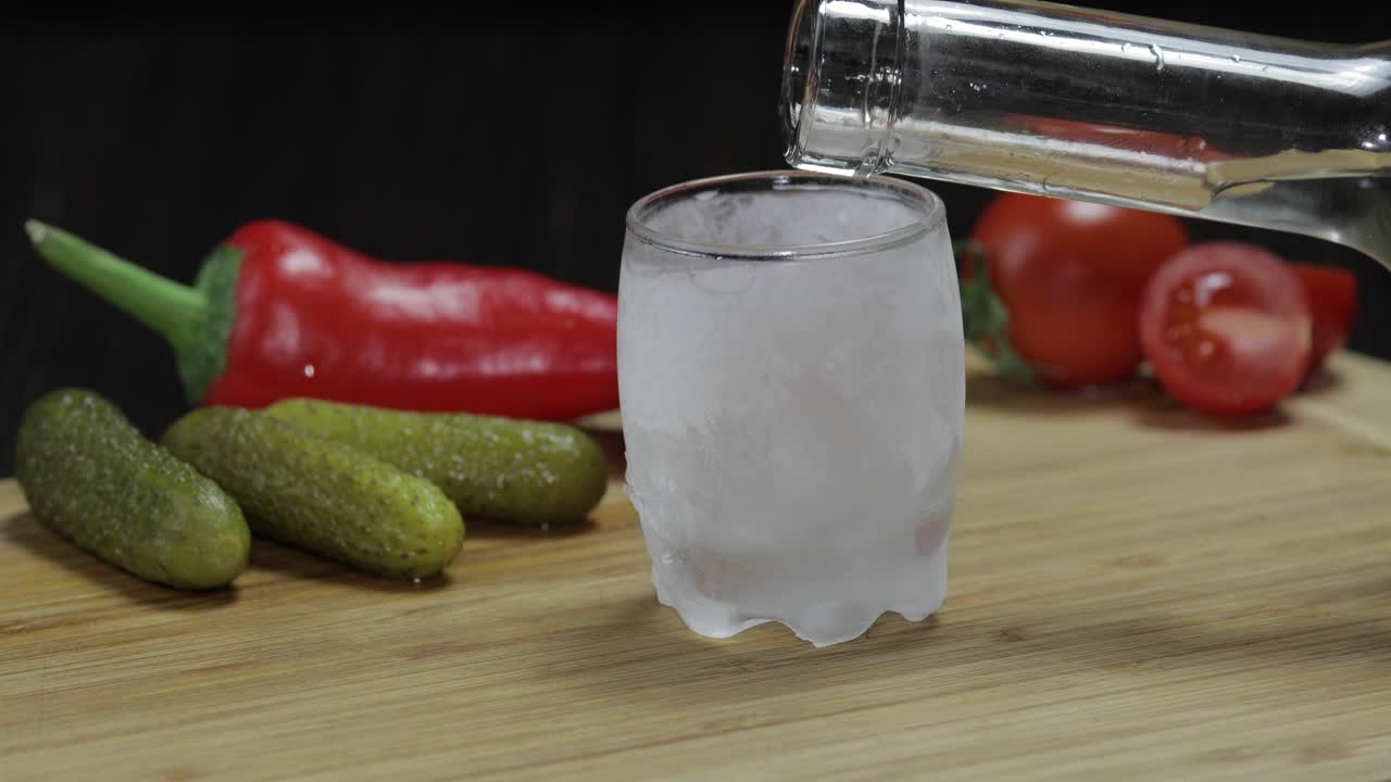 человек кладет ледяной стакан, наполняет его водкой и поднимает стакан.