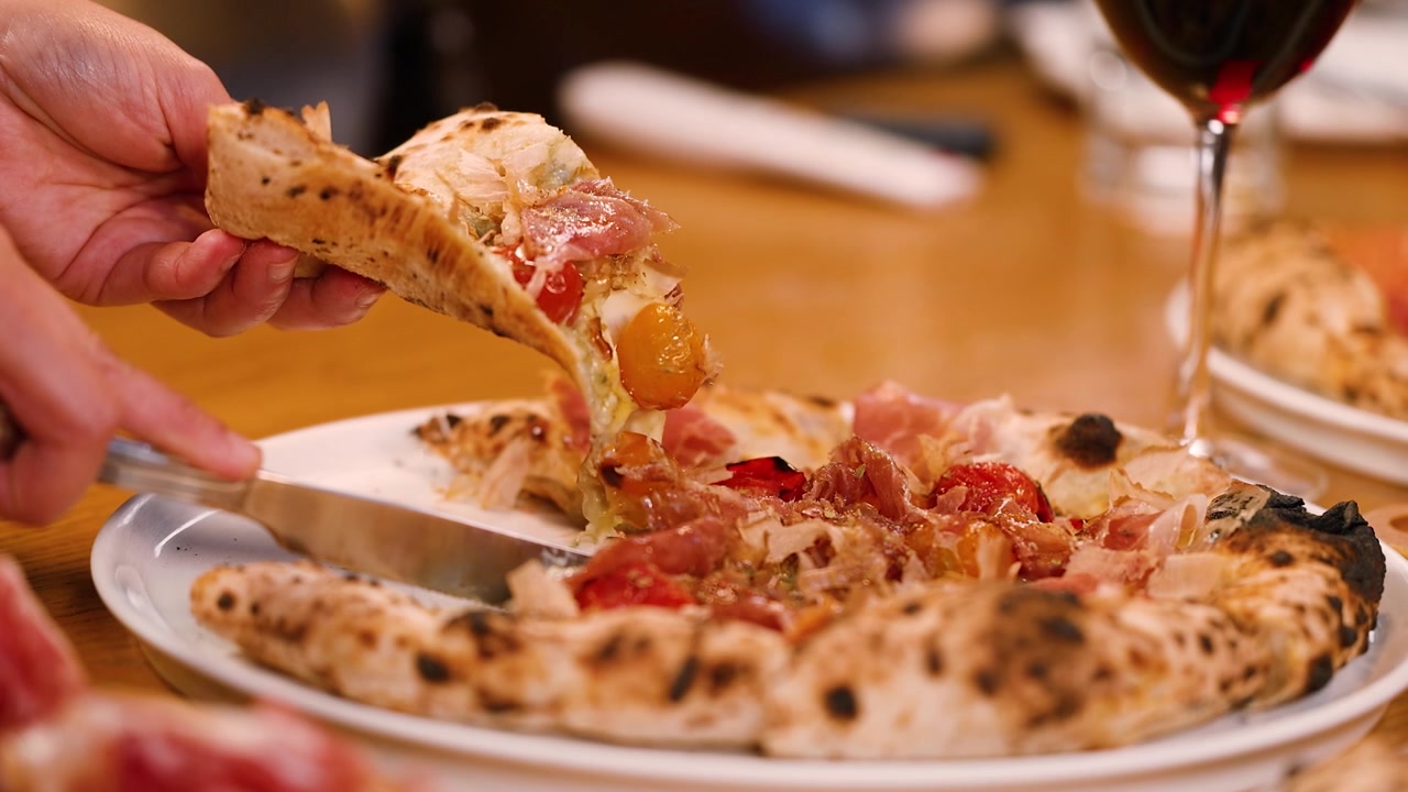 Una persona usa un coltello per tagliare e sollevare una fetta di pizza gourmet con burrata.