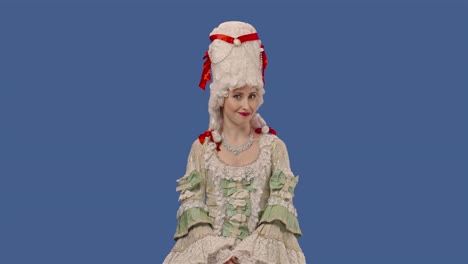 retrato de una dama de la corte en un vestido de encaje vintage blanco y una peluca está masticando chicle y soplando burbujas. mujer joven posando en el estudio con fondo de pantalla azul. primer plano. cámara lenta lista 59.94fps