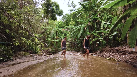 static shot of two tourists crossing barefoot a water stream in the middle of the jungle of northen area of thailand during coronavirus outbreak