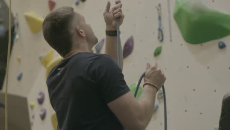 man securing rope before climbing at indoor gym