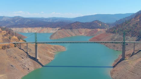 disturbing aerial over drought stricken california lake oroville with low water levels, receding shoreline and large bridge crossing