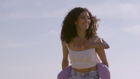 beautiful young american mother carrying her little daughter on her back while spending time at the beach on a sunny day