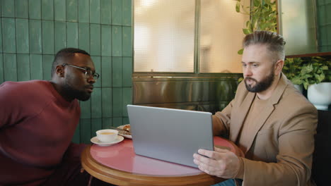 Multiethnic-Businessmen-Discussing-Project-on-Laptop-in-Cafe