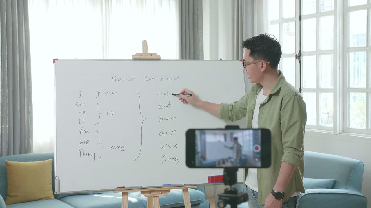 Asian Male Teacher With Glasses Shoots Video By Smartphone Camera While Teaching English At Home