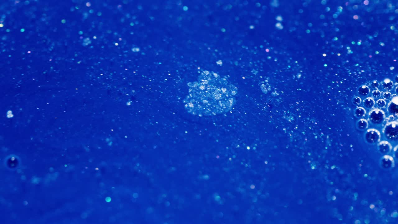 Mixing blue ink with bubbles and particles creating an abstract macro shot