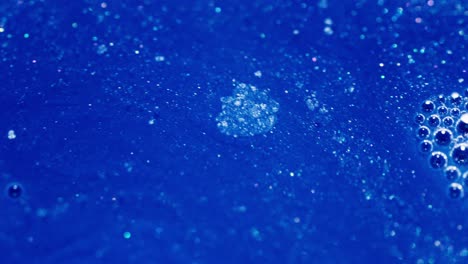 mixing blue ink with bubbles and particles creating an abstract macro shot
