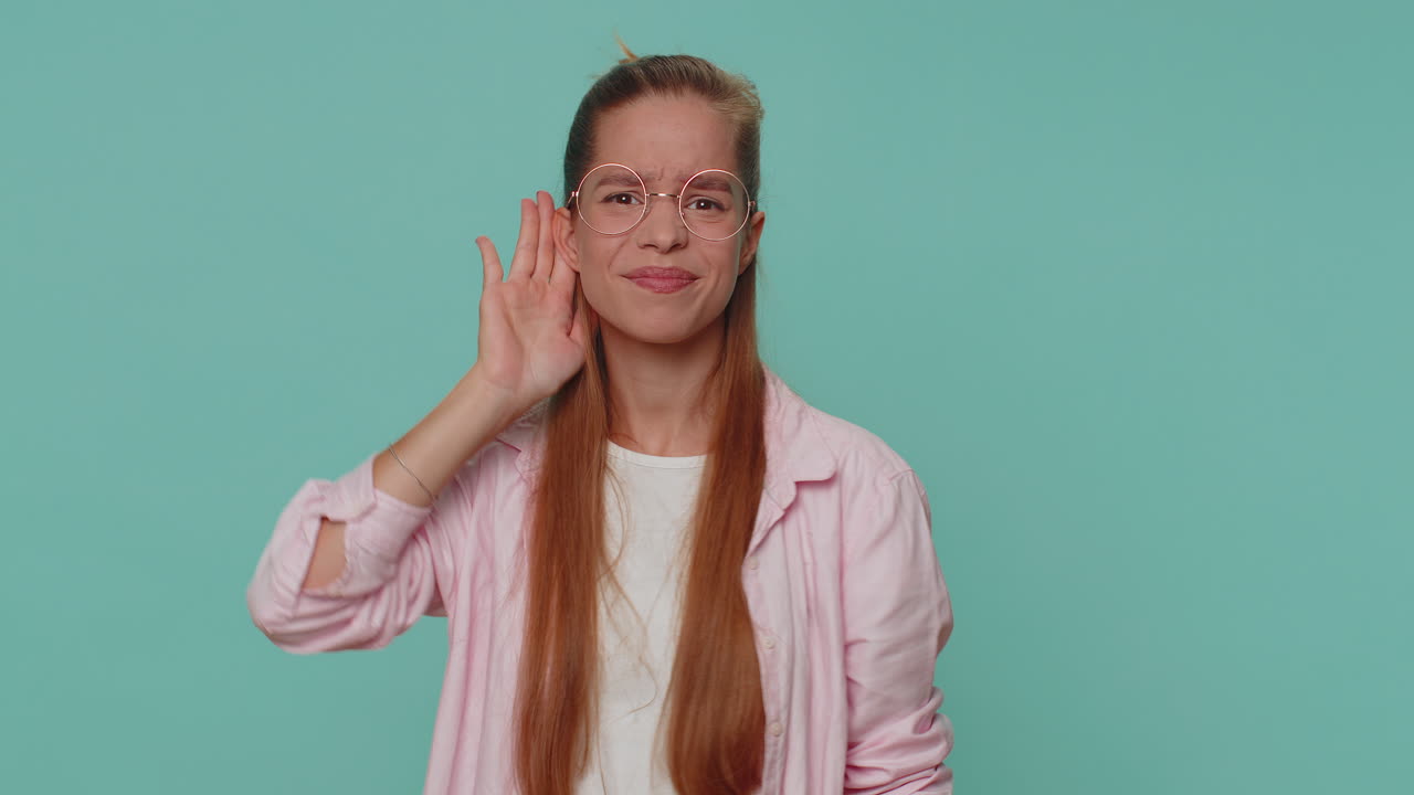 niña adolescente tratando de oírte mirando confundido y fruncido el ceño, manteniendo el brazo cerca de la oreja para una voz más alta
