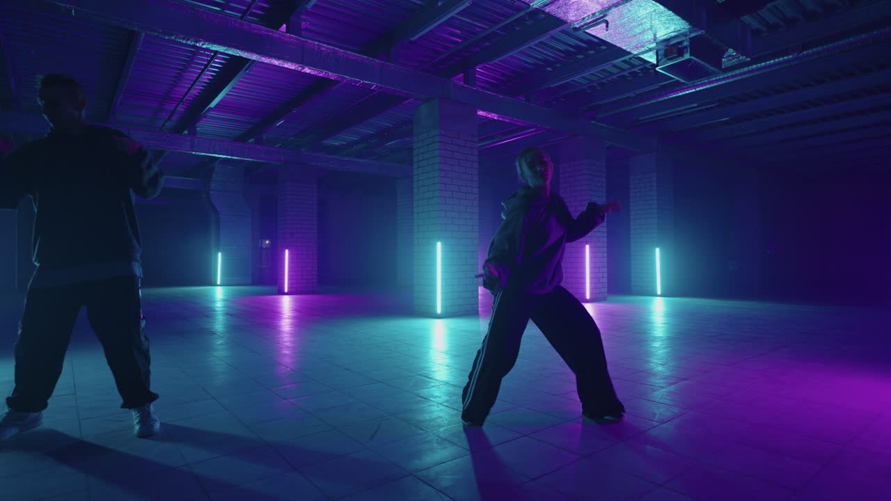 dos bailarines profesionales de estilo femenino y masculino realizan una rutina de baile de hip hop en un entorno de estudio de producción virtual. mujeres y hombres hip hop se mueven en un estudio oscuro con humo e iluminación.