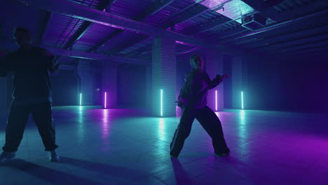 Two-Stylish-Professional-Female-and-male-Dancers-Performing-a-Hip-Hop-Dance-Routine-in-Virtual-Production-Studio-Environment.-Women-and-men-hip-hop-moves-in-dark-studio-with-smoke-and-lighting.