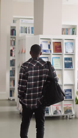 man walks across public library hall. african american visitor with backpack comes for scientific books to literature storage. reader at bookstore