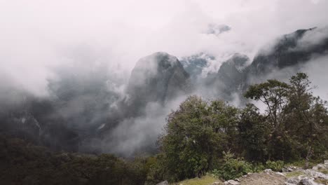 Foggy Clouds Engulfing Andes Mountains Near Machu Picchu Incan Citadel In Cusco Peru. Aerial Tilt-up Shot