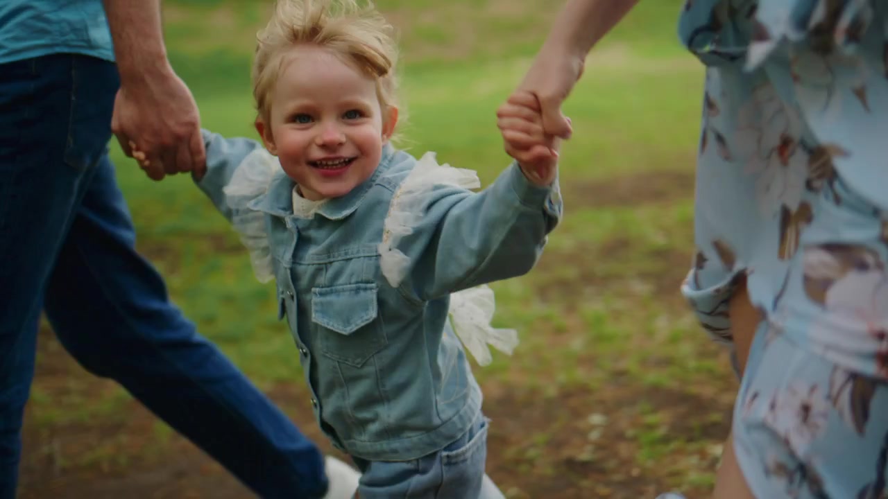 Young child laughs joyfully, held by two adults outdoors. Family moment captures playful, carefree energy. Perfect for themes like family bonding, childhood happiness, or outdoor adventures