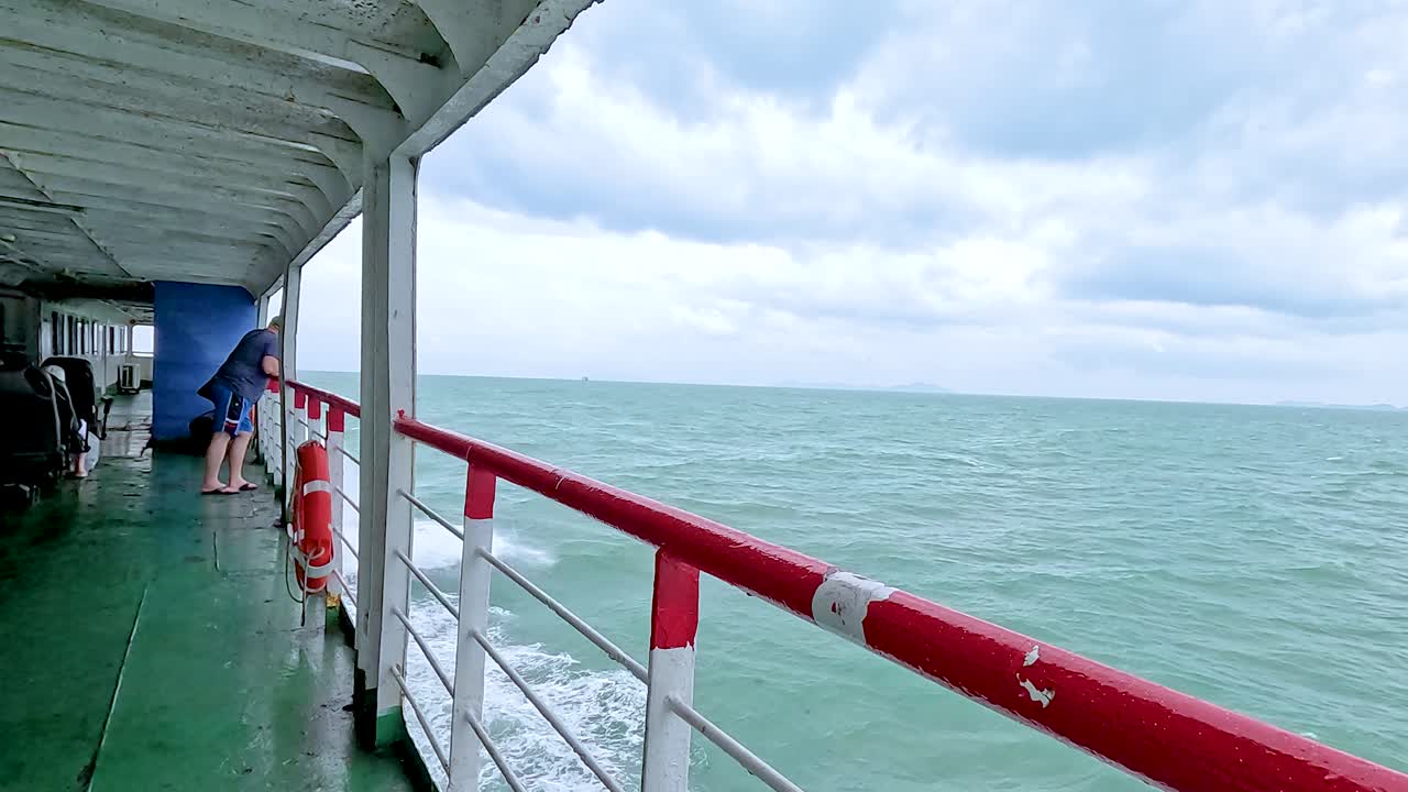 A ferry glides through turquoise waters under cloudy skies near Koh Samui, Thailand, capturing serene ocean views and distant islands
