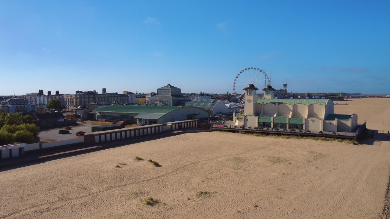 Great Yarmouth Wellington Pier and beach low circling aerial drone shot, Norfolk coast. This is a traditional British seaside town with amusement attractions and arcades