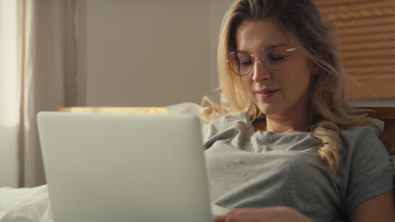 Caucasian woman using the laptop and lying in bed at home in morning