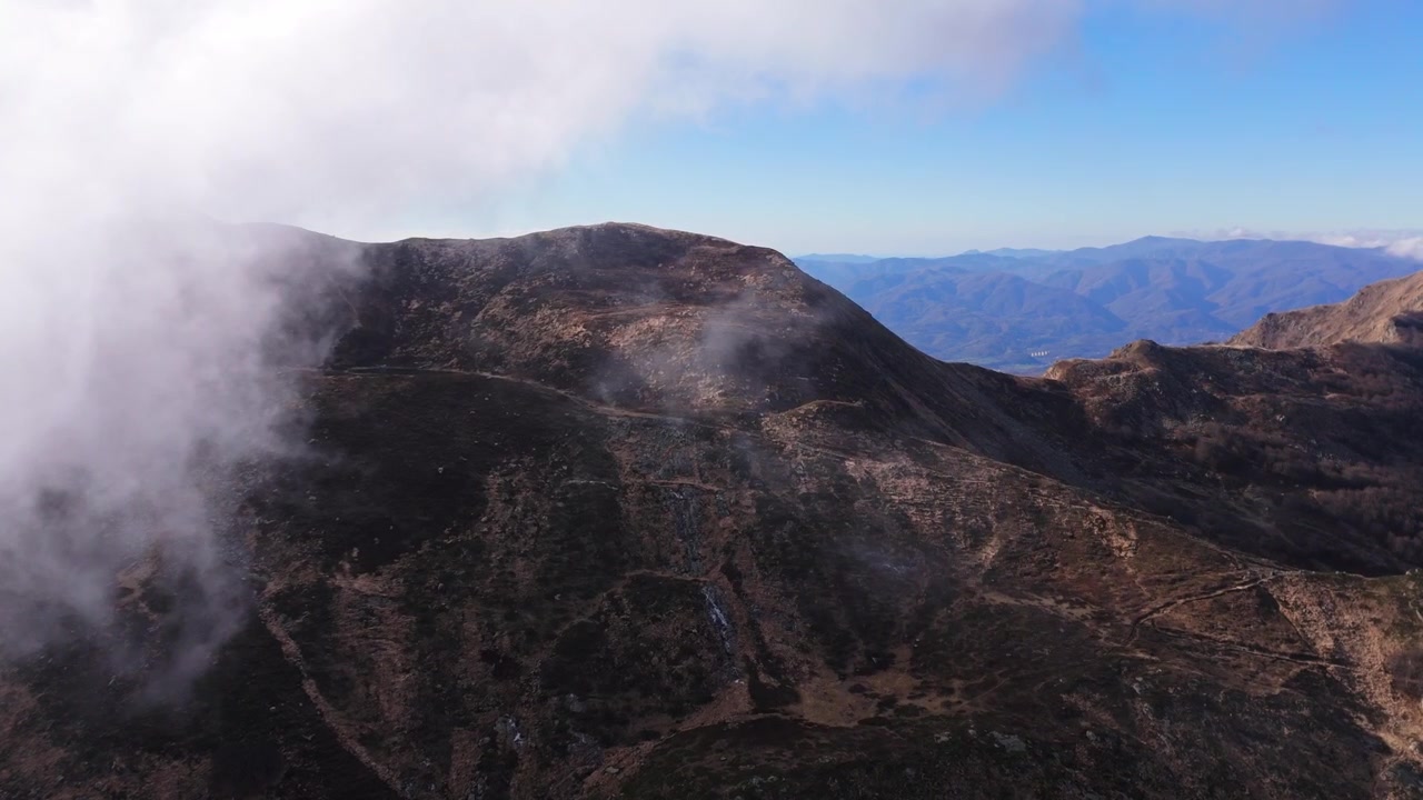 Ripresa aerea cinematografica del terreno montuoso accidentato ai Lagoni, con fitte nuvole bianche che si muovono sopra le vette rocciose sotto un cielo azzurro limpido. Ideale per documentari sulla natura e sui viaggi