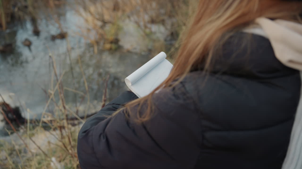 Una donna prende nota delle piante. Un'osservatrice documenta la flora delle zone umide. Una donna delicata registra le osservazioni sulle piante della palude. Esamina e documenta meticolosamente i dettagli della vegetazione delle zone umide in un taccuino.