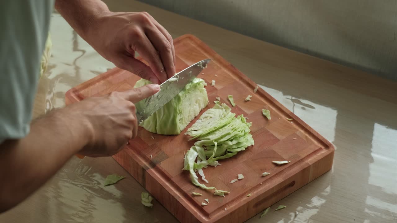 Man Thinly Slicing Cabbage On Wooden Chopping Board. - closeup shot