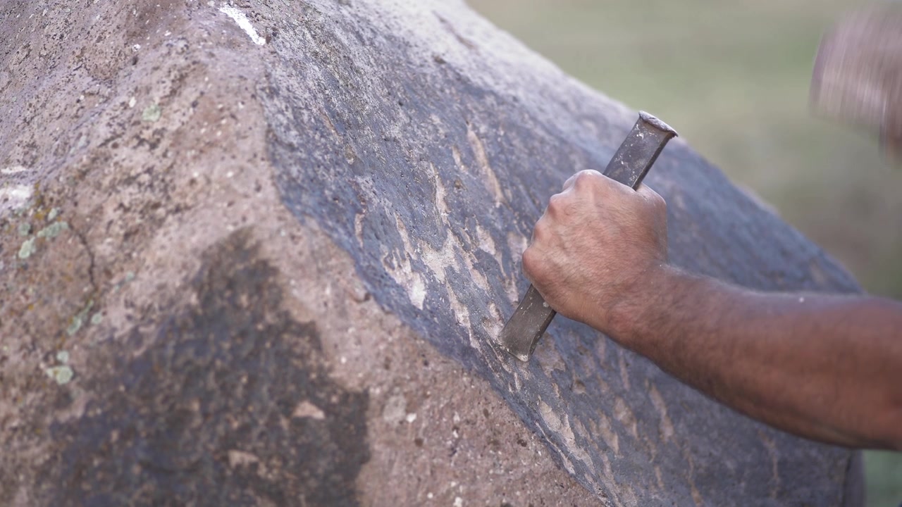 Artisan Carving Petroglyphs into Large Stone with Chisel and Hammer