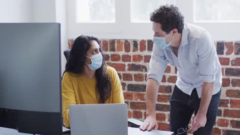 hombre y mujer con máscaras faciales trabajando juntos en la oficina