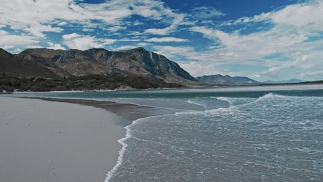 a stunning scene as ocean waves roll into a lagoon estuary with mountains in the distance