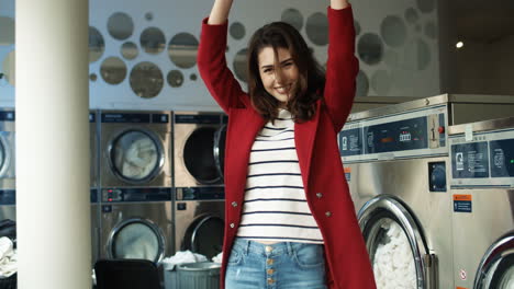 joyful pretty and stylish woman having fun and dancing in laundry service room while machines washing working