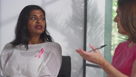 Women-Wearing-Pink-Breast-Cancer-Awareness-Ribbons-Meeting-And-Talking-At-Therapy-Support-Group-For-Cancer-Treatment-Patients-With-Counsellor-1