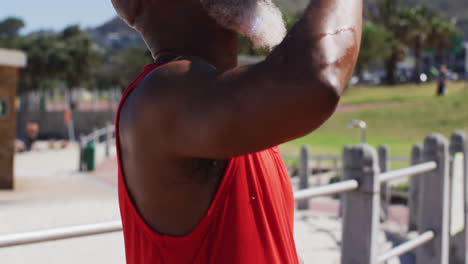 homem afro-americano sênior com basquete bebendo água na quadra perto da praia